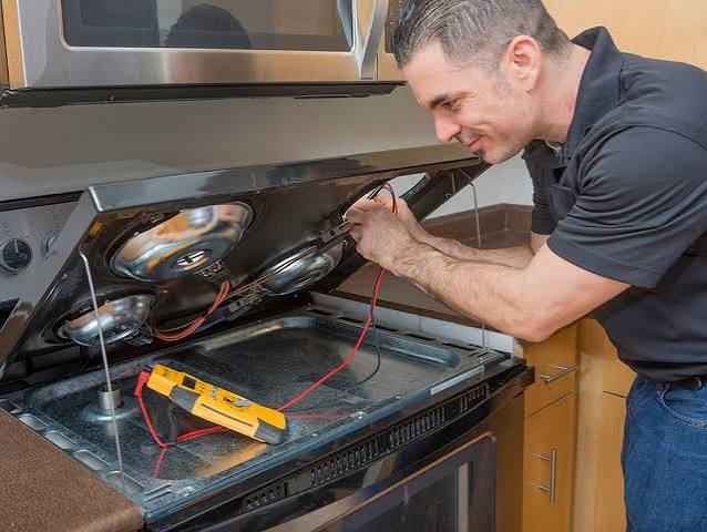 Appliance repair technician testing a stove with a multimeter
